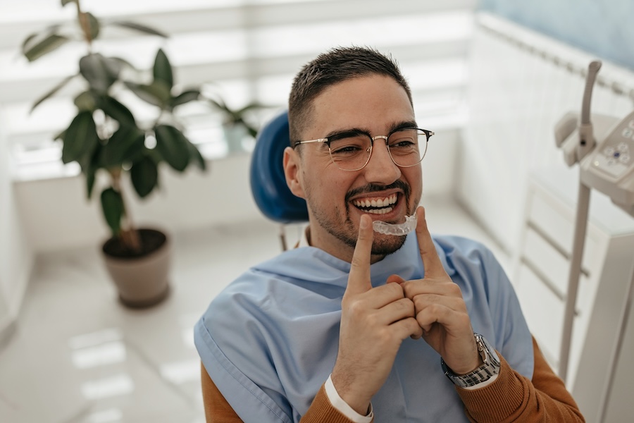 man in dental chair holding clear aligners, Invisalign